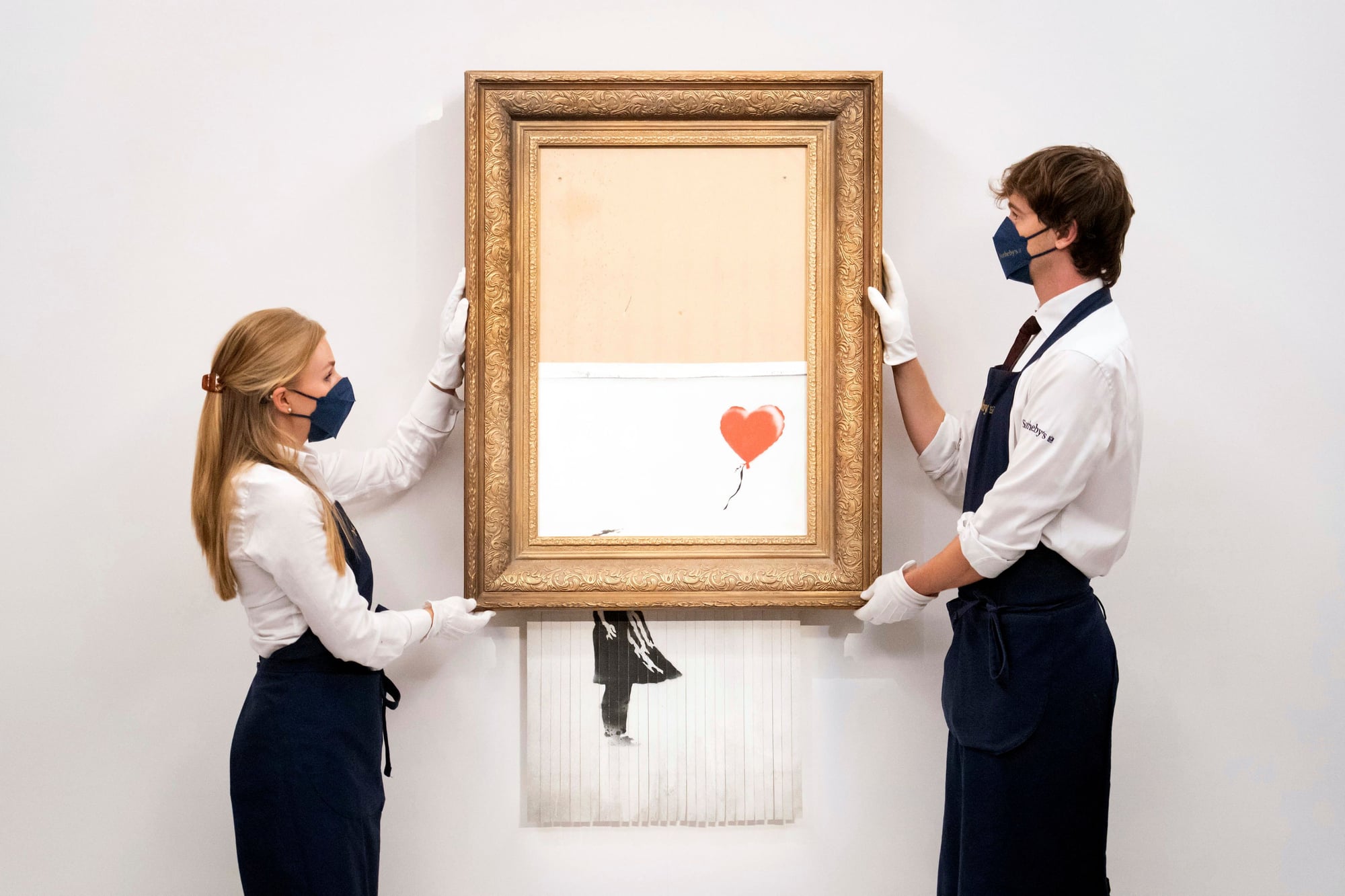 Sotheby's employees hold up Banksy's half-shredded 