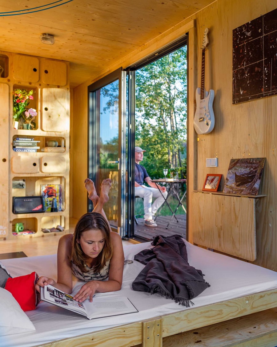 Couple lounges around the Gaia Off-Grid Container House with the folding bed down and all the doors open.