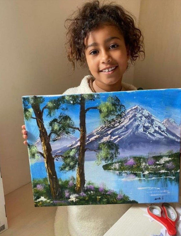 Kanye's daughter North West proudly holds up a Bob Ross-style painting she made. 