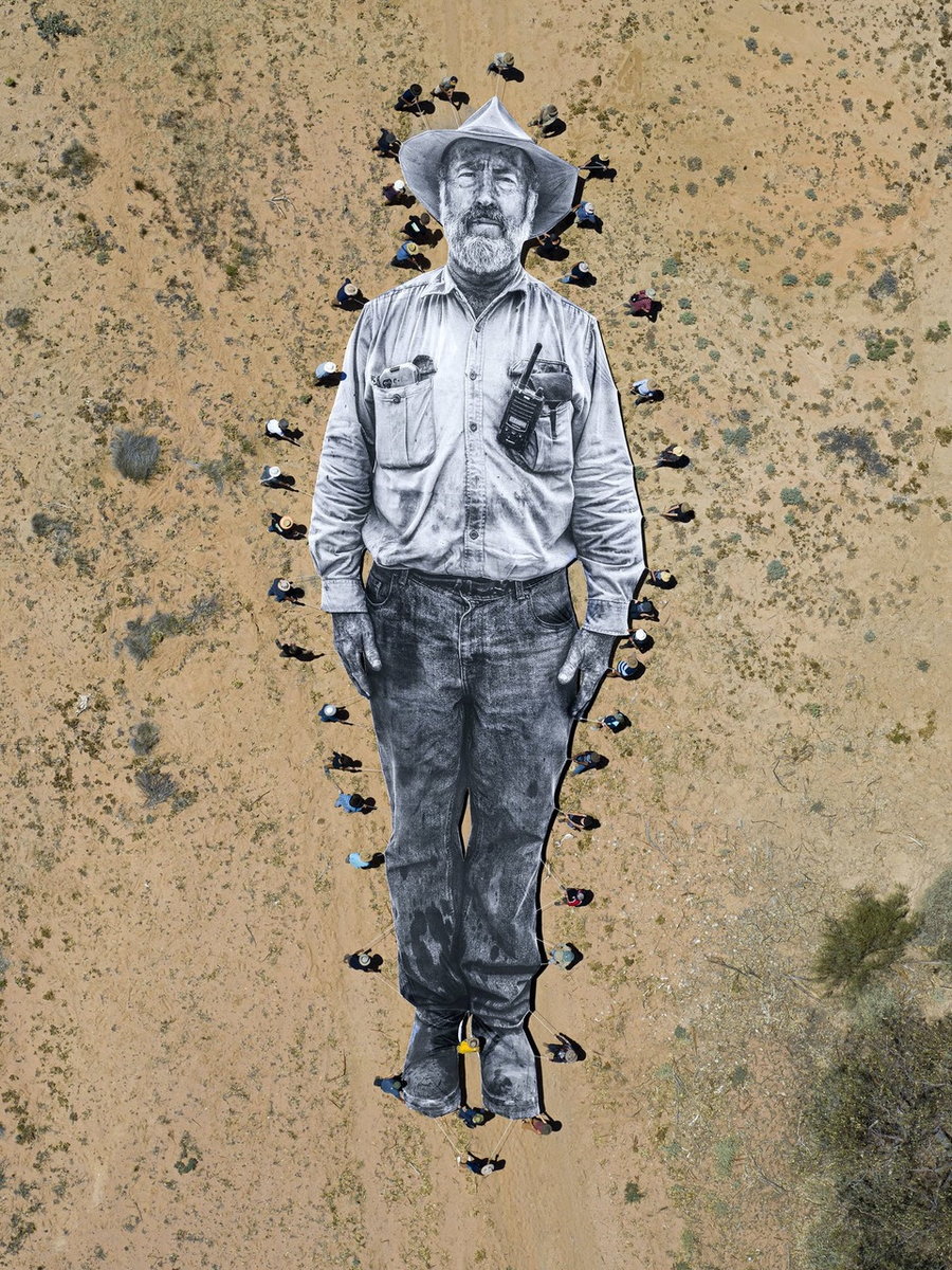 Australian farmers and indigenous peoples carry a massive portrait of orchardist Alan Whyte through the desert as part of French artist JR's 