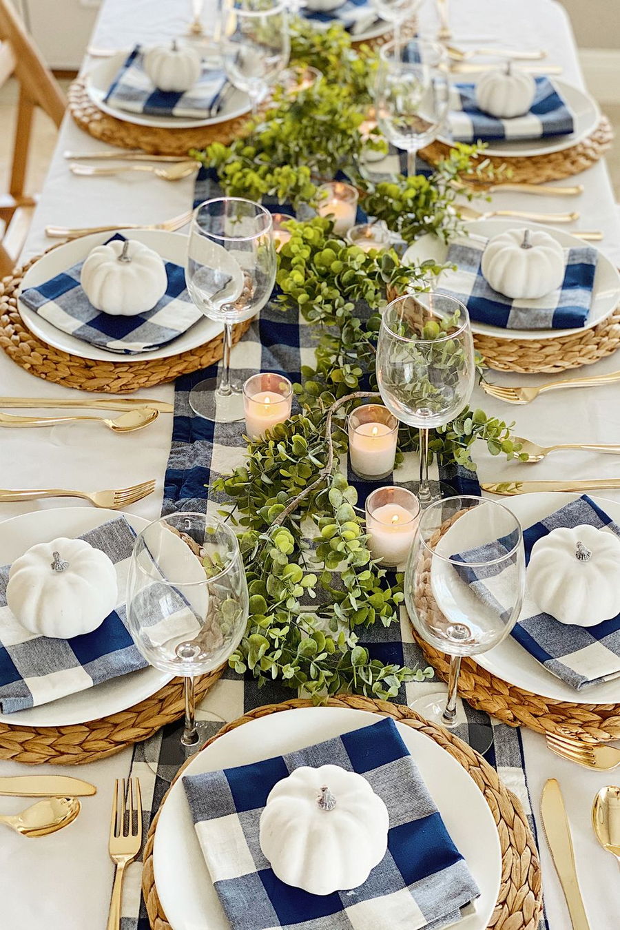 Gingham napkins and small white pumpkins arranged all around a Thanksgiving table. 