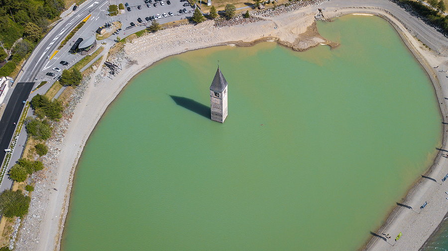 Far-off aerial view of the Curon bell tower emerging from the surface of Lake Resia.