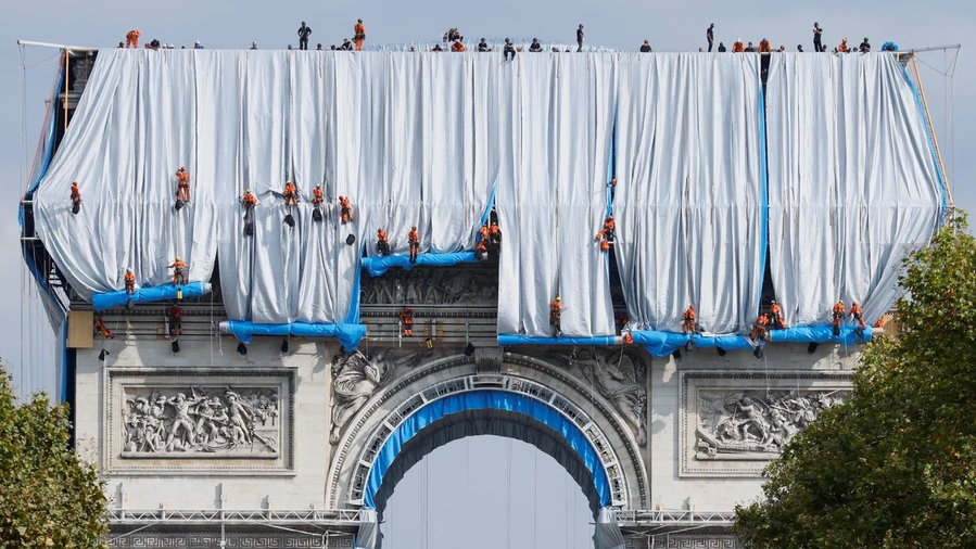 Workers roll out long strips of fabric over Paris' famed Arc de Triomphe. 