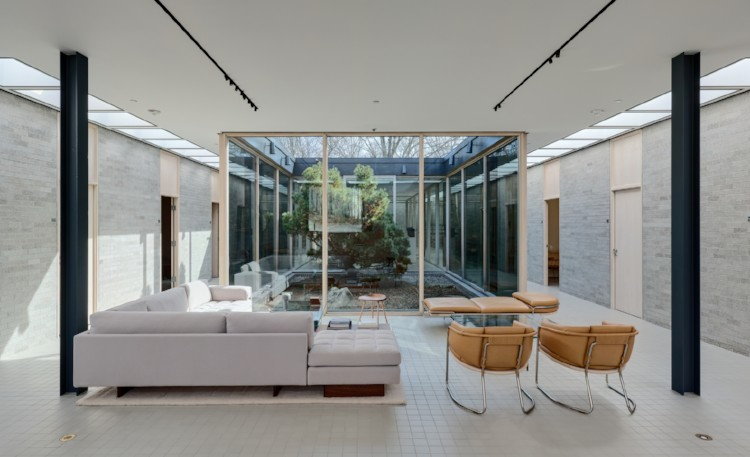 a stone and glass space with modern furniture next to a courtyard with a pine tree