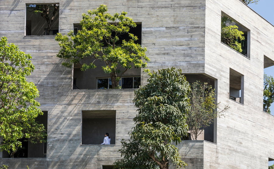 Large trees of all shades of green burst out from openings in the villa's exterior facade.