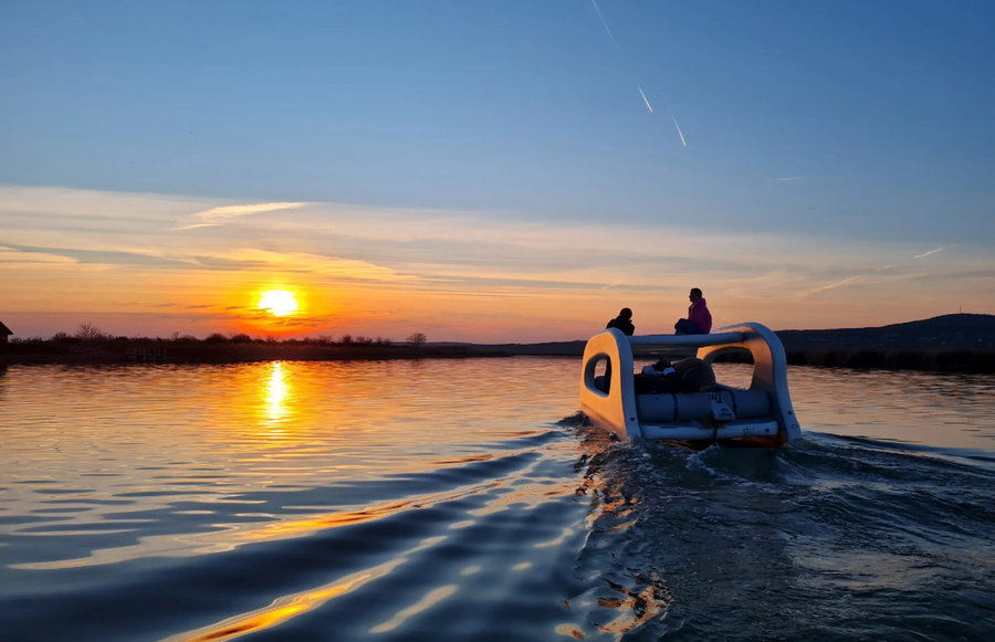 Portless Catamaran cruises through the water at sunset.