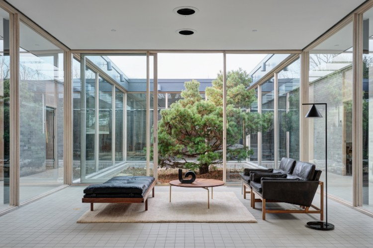 a glass waiting room next to a courtyard with a pine tree