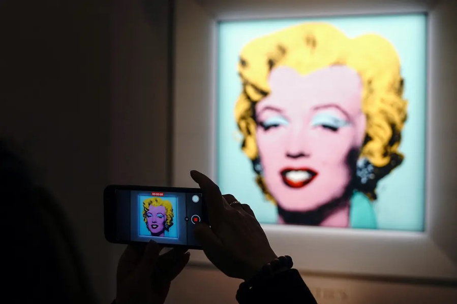 Person photographs Andy Warhol's Shot Sage Blue Marilyn portrait on display at auction.
