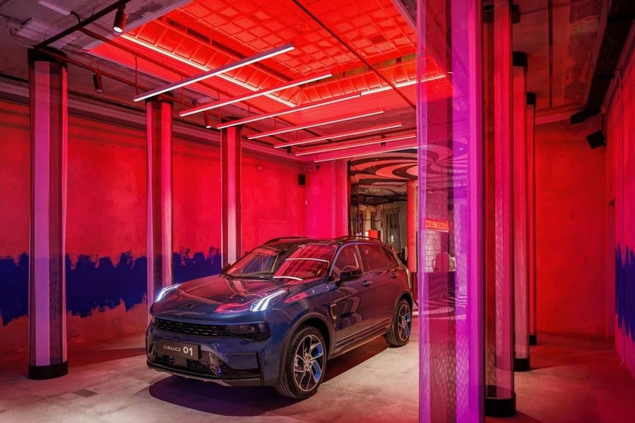 Bold red and purple lighting shines down on Lynk & Co's stylish, smart 01 hybrid vehicle at the company's Milan club.