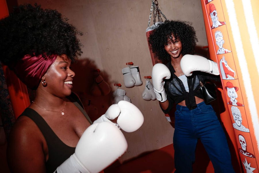 Women visiting a Hermèsfit pop-up gyms don white boxing gloves as they prepare to enter the ring.