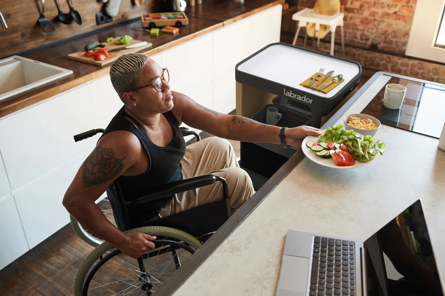 Labrador Retriever Robot Shelf brings person in a wheelchair their lunch.