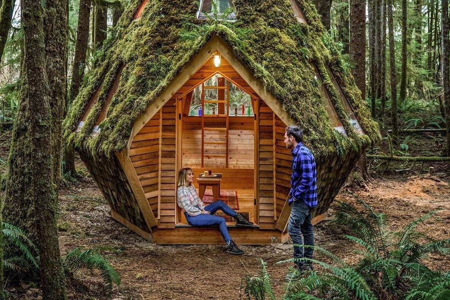 Jacob Witzling and Sara Underwood laugh and talk on the porch of a diamond-shaped cabin on their Cabinland development.