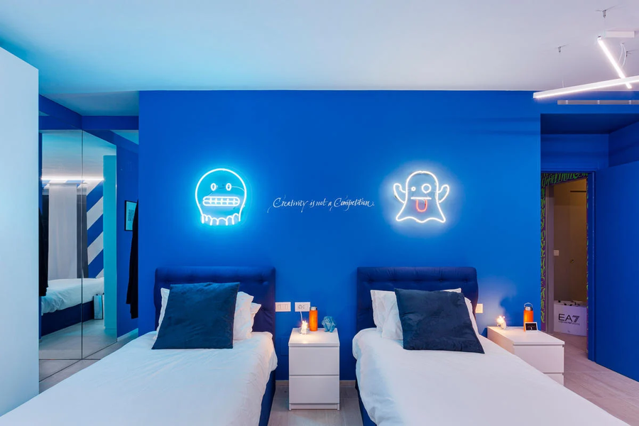 This bright blue bedroom in the Defhouse uses bold neon lighting fixtures to spice up an otherwise relatively simple decor. 