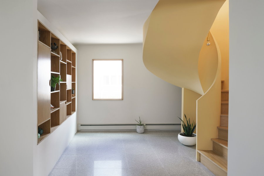 Yellow spiral staircase bleeds into the original home's calm white interiors from the experimental addition above.