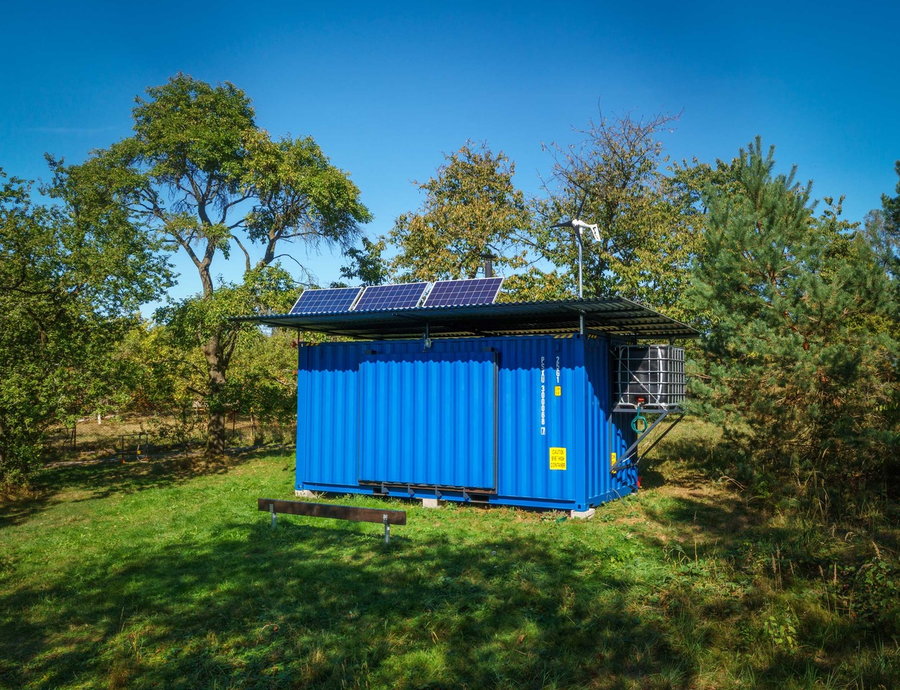 A fully closed up Gaia Off-Grid Container House, with the solar panels and wind turbine visible on the roof. 