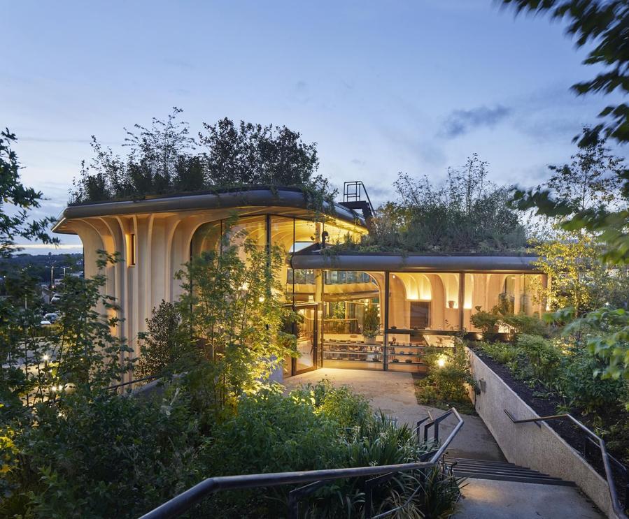 Thomas Heatherwick's planter-shaped health center buildings give off a cozy glow in the twilight.