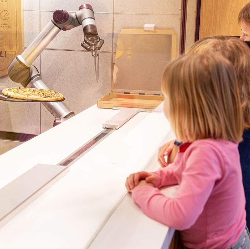 Little girls watch in awe as the Pazzi robotic arm prepares their pizza from start to finish.
