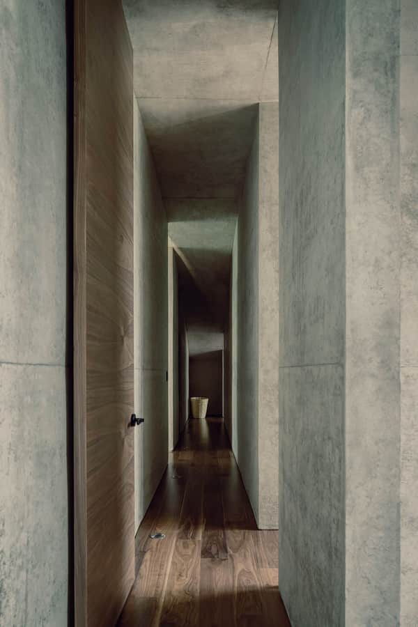 Minimalist concrete hallway inside the Hill in Front of the Glen home, with warm wooden accents on the floor and doors.