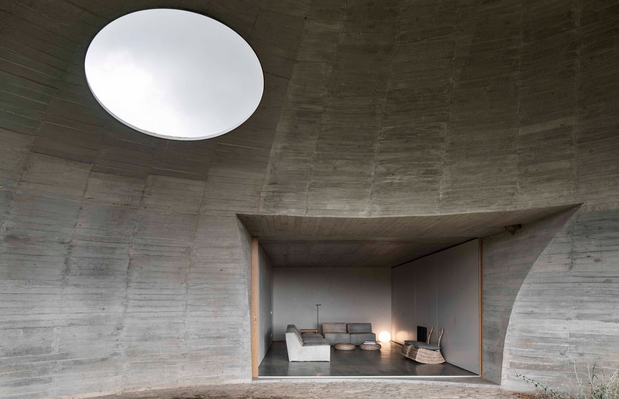 The stark concrete living area inside the underground home sits nicely beneath a large skylight. 