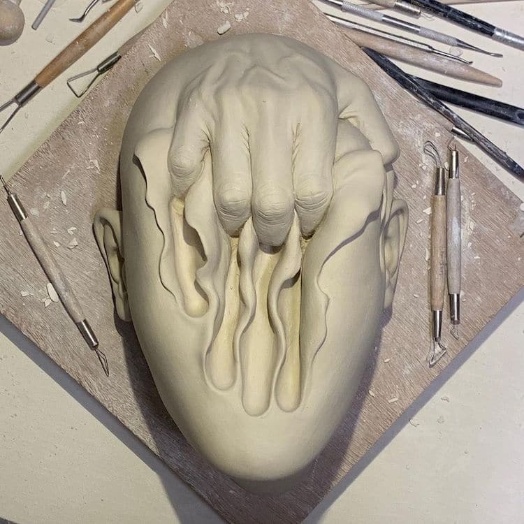 Surreal ceramic by Johnson Tsang shows a hand clawing through a face.