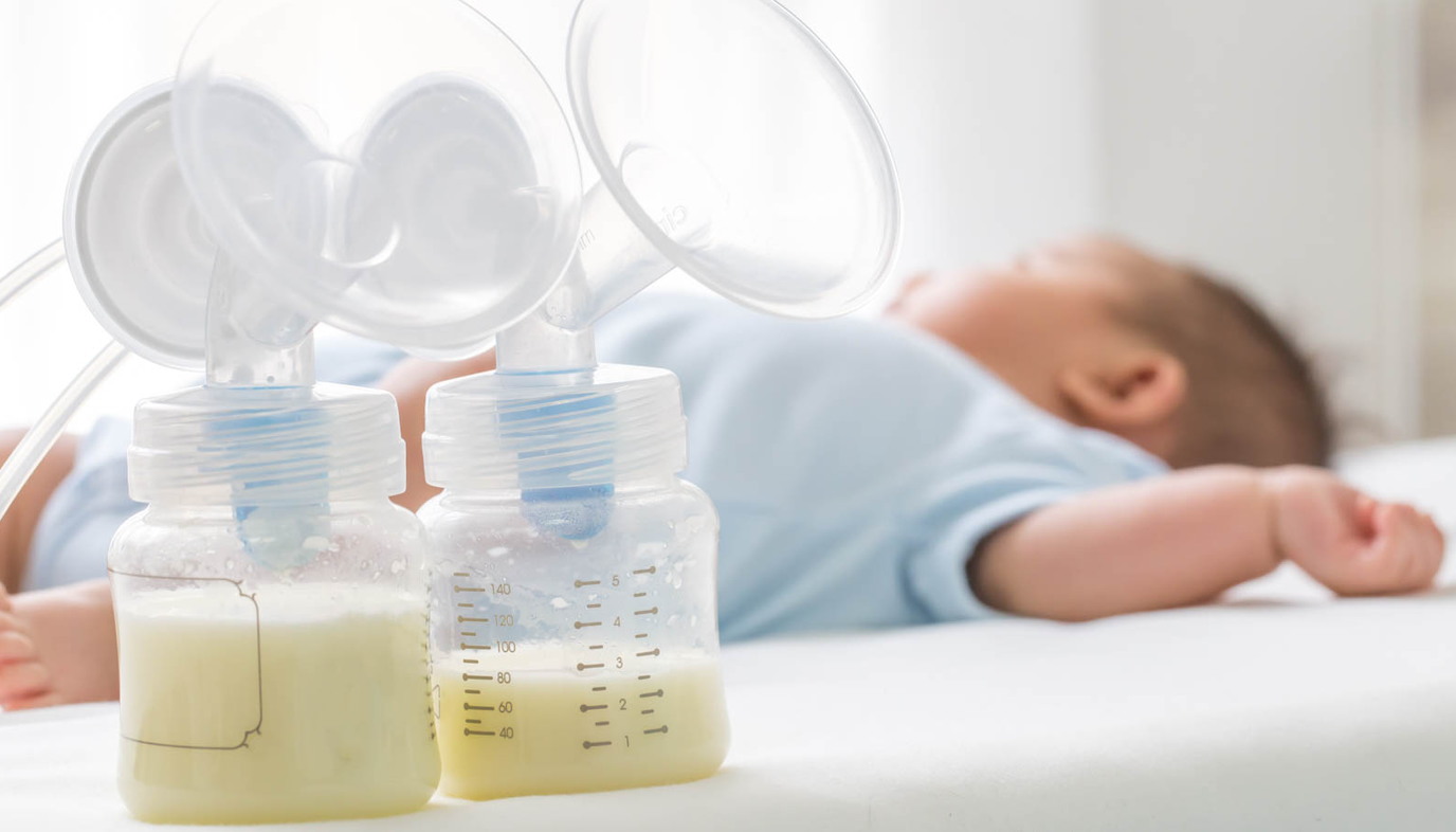 baby sleeping next to bottles of pumped breast milk