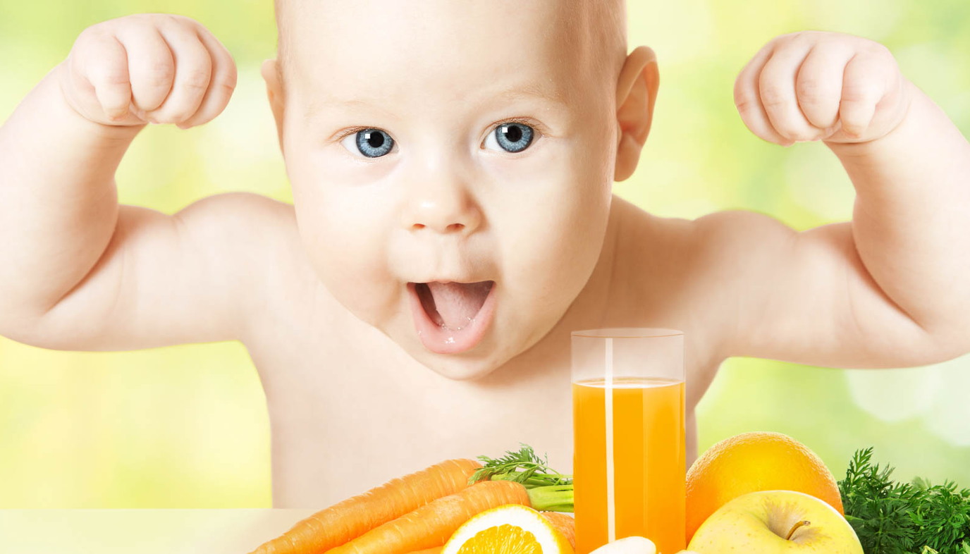 Baby with arms raised near fruit, vegetables, and juice