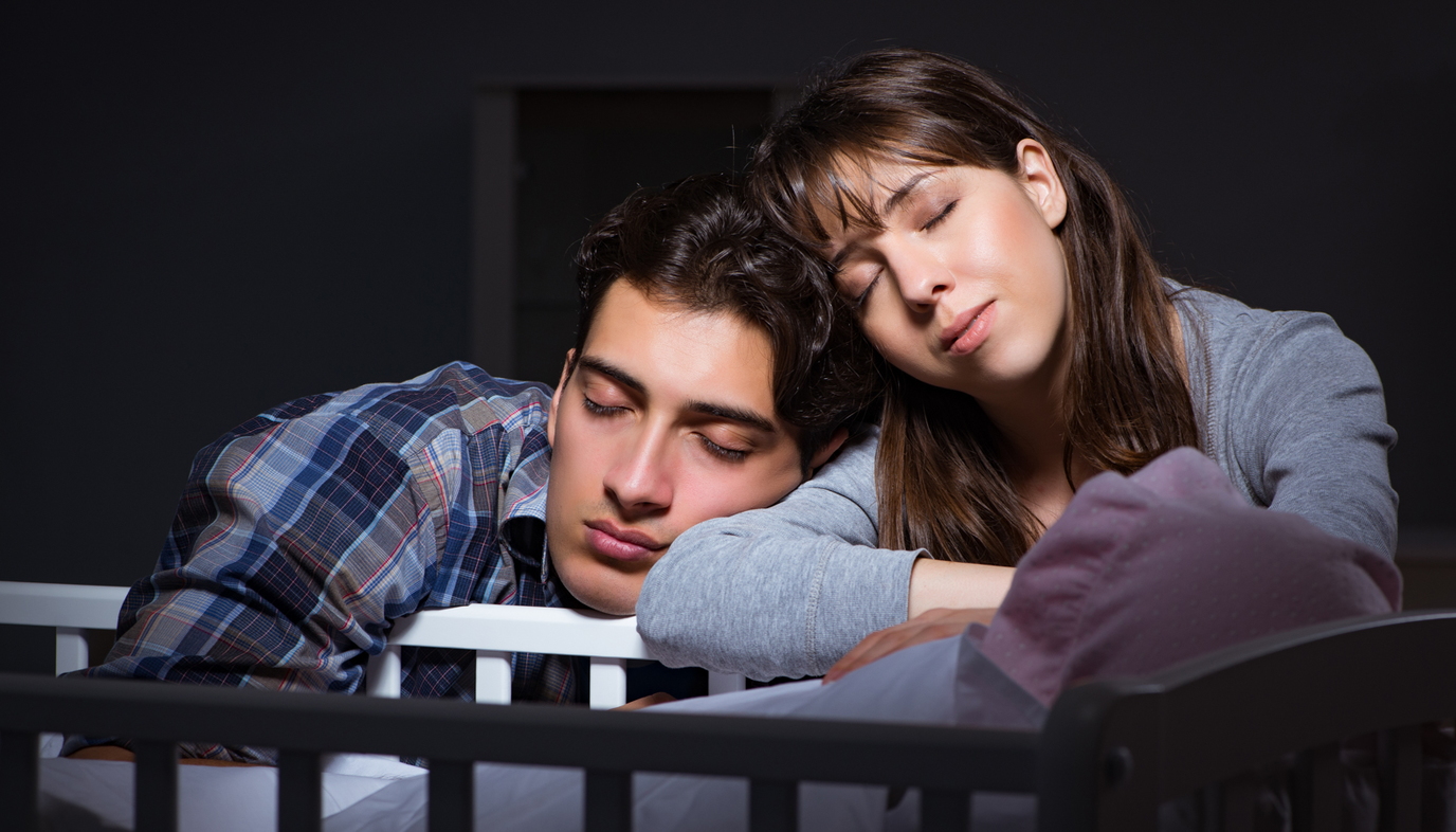 new parents sleeping by baby's crib