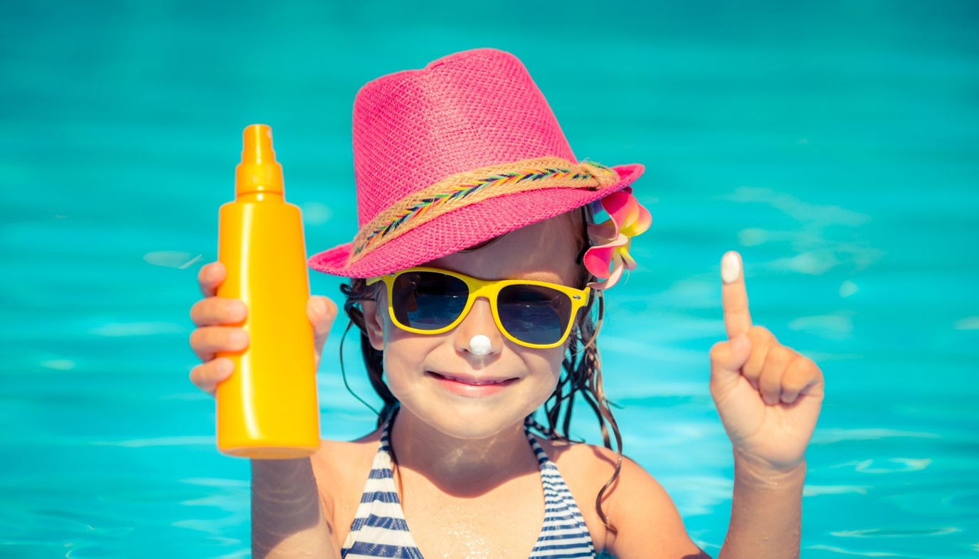 girl in the pool holding bottle of sunscreen