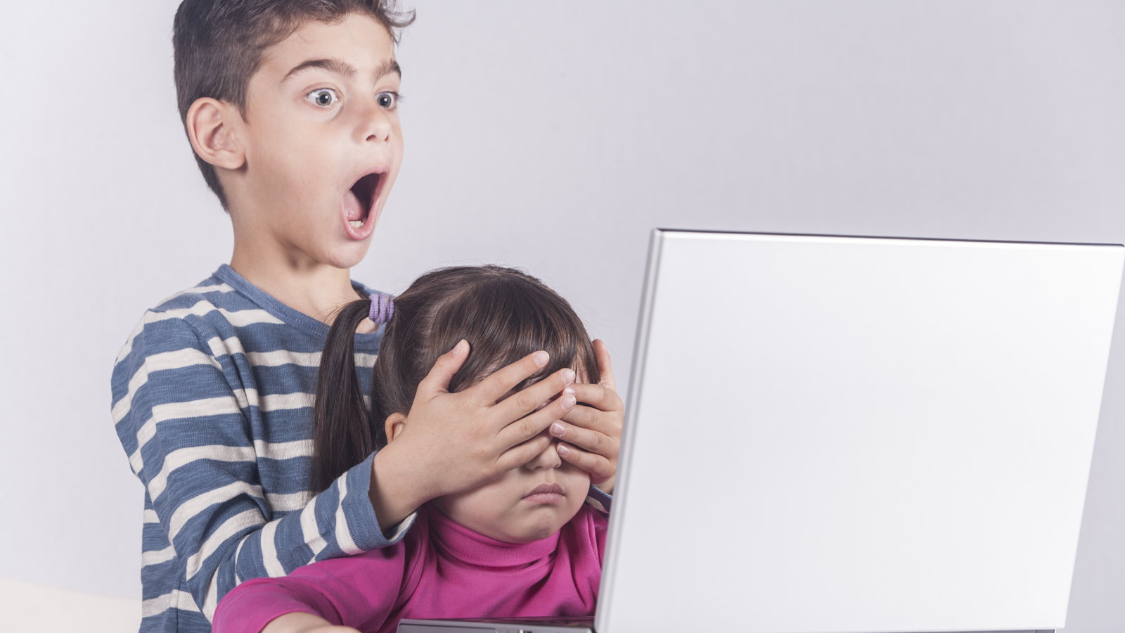 boy covering sister's eyes while looking at laptop