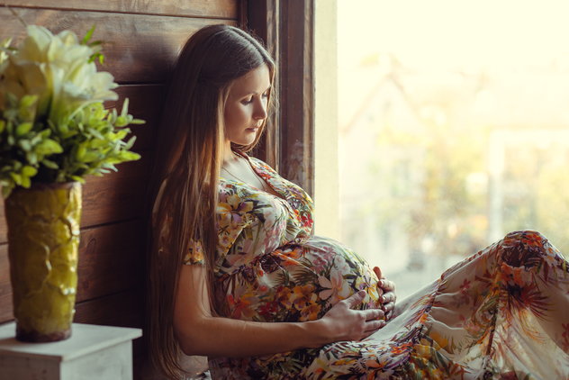 A pregnant woman sitting by a window. 