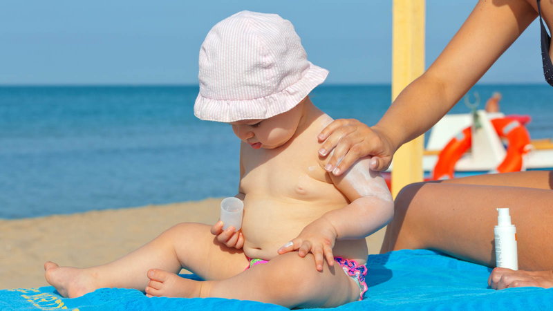 mom putting sunscreen on baby at the beach