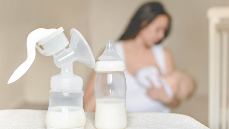 bottle of breast pump with mom in the background breastfeeding