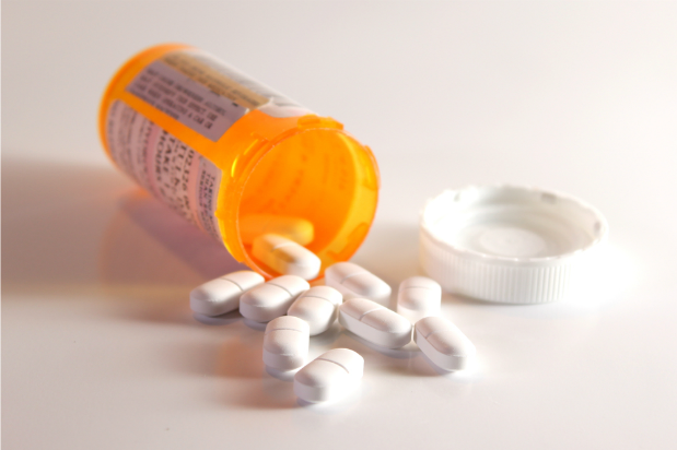 orange-colored open bottle of pills spilling over contents on white surface