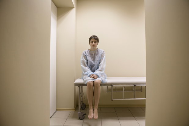 A woman sits on an exam table at a facility that practices the harm reduction model of addition treatment.