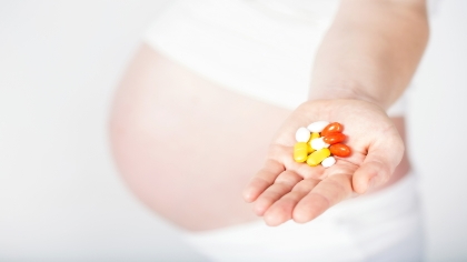 An expectant mother holds out a handful of vitamin supplements. 