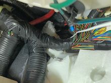 Coat-hanger penetrating the grommet above and behind the "Pi Harness" in the right-hand footwell of an '06 LHD DB9 Volante (it's the white wire below the green wire on the right side of the image)