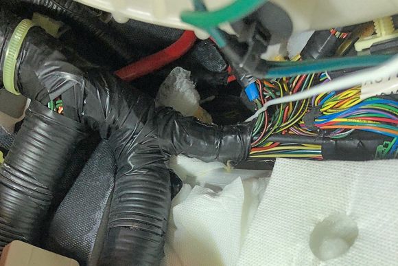 Coat-hanger penetrating the grommet above and behind the "Pi Harness" in the right-hand footwell of an '06 LHD DB9 Volante (it's the white wire below the green wire on the right side of the image)
