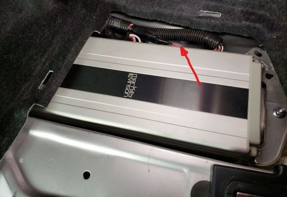 Right/Passenger's side vent is behind the harness, arrow points to its top rear edge.  The aft amp bracket's 10mm nut is at right, there is a similar nut under the carpet to the left.  Once the nuts are removed, the entire amp can be removed and/or rotated out of the way.  Make sure to place the harnesses on *top* of the plastic cable tray under the amp before reinstalling.  AMHIK.  