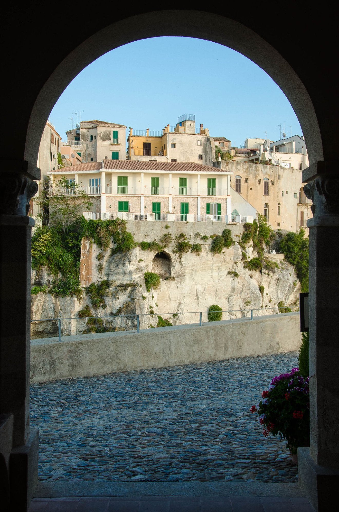 Arch view from inside tiny onsite chapel out to main center of Tropea. Nearby sign: THE CHRISTIAN DRESSES PROPERLY BEFORE ENTERING HERE. NO __________(long list of unacceptable attire).