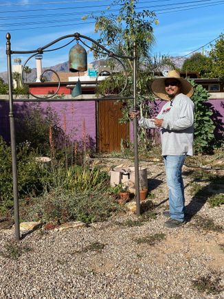 Here is our bell in the headboard we bought at a yard sale a couple of years ago in hopes of using it in the garden., with the handy guy who saw it and thought it would be much better and more interesting than the rebar we were thinking about. We love it and it fits into sensibility of our garden.
He cut away some of the design to make the space for the bell, which is made by an artisan on the Santa Fe-Taos road out of old propane tanks.
We’ll grow some vines on the posts. Maybe scarlet runner