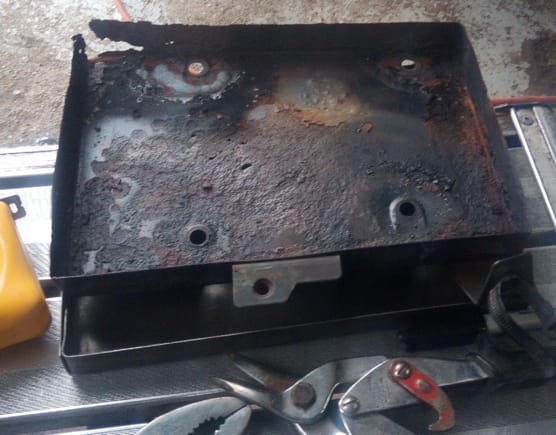 Rusty old battery tray with holes in the bottom of the tray